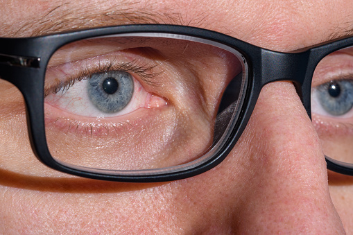 glasses with black frames on the nose of a man with blue eyes, macro close-up