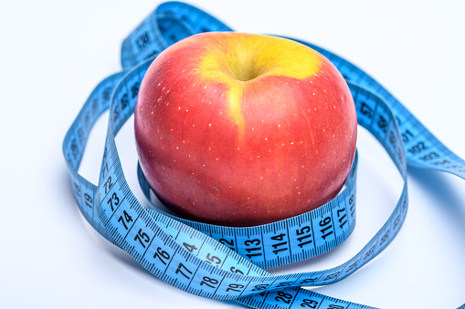 beautiful red ripe apple on a white background wrapped with a measuring tape as a diet metaphor