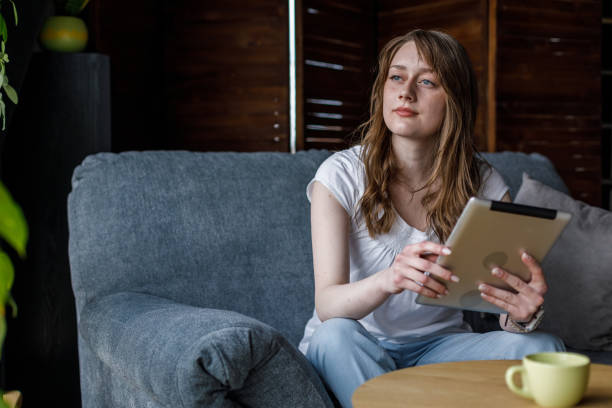 istock Young woman relaxing on the sofa, using digital tablet and contemplating 1488099817
