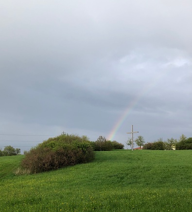 A big cross in the countryside and a rainbow over it