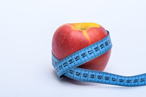 One red ripe apple wrapped with a tape measure on a light background