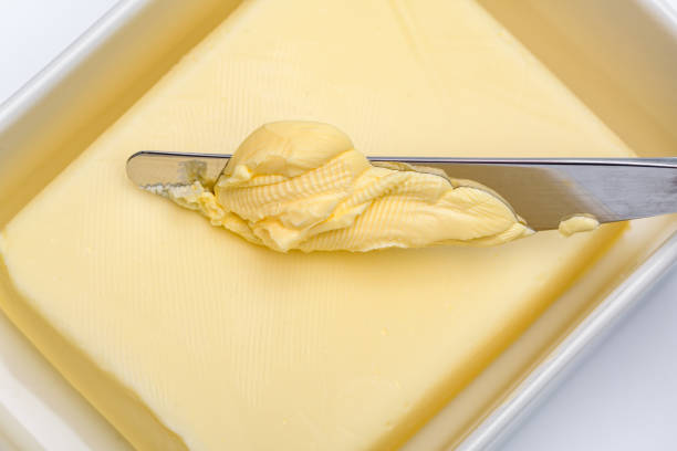 A DSLR photo of butter block in white ceramic butter container. The container cover sits on the background 