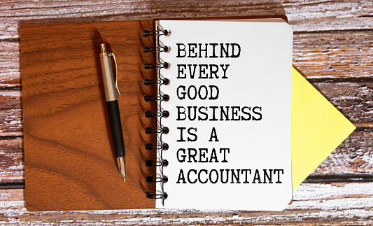 Financial quote Behind Every Good Business Is A Great Accountant handwritten on yellow sticky note on laptop keyboard.