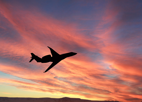 Silhouette of a private executive jet against a dramatic sunset sky. No people. Travel concept.