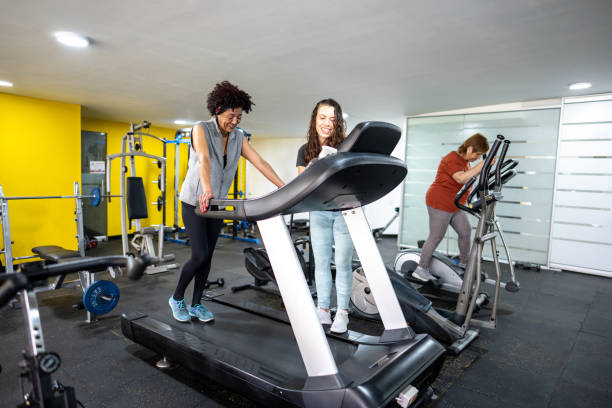 Female fitness instructor helping senior woman on treadmill in the gym
