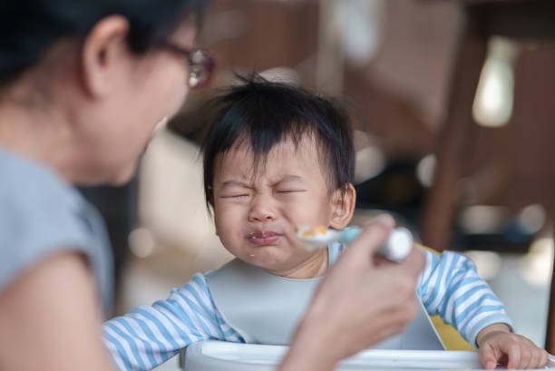 istock Cute baby boy refusing to eat food and crying while his mother feeds him. 1488118943