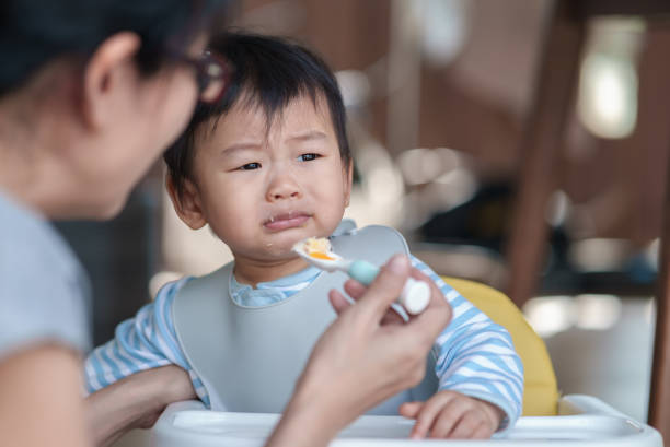 istock Cute baby boy refusing to eat food and crying while his mother feeds him. 1488118945