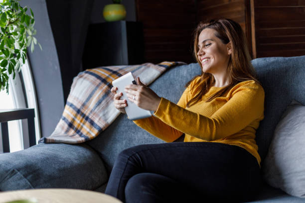 istock Cheerful young woman lounging on the sofa and using digital tablet 1488121234