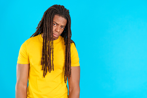 Sad latin man with dreadlocks looking at camera in studio with blue background