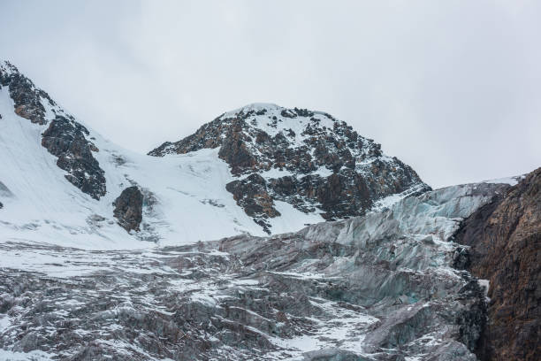 istock Dramatic landscape with large icefall on glacier under snow mountain peak in gray cloudy sky. Sharp rocks and beautiful glacier with icefall in high altitude. Gloomy scenery in mountains in overcast. 1488123833
