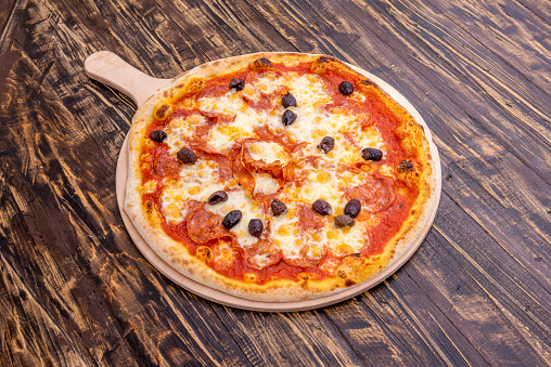 Super diavola pizza with black olives, spicy pepperoni, mozzarella cheese and tomato on dark wooden table.