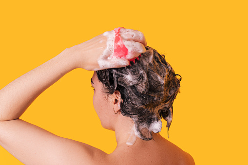 Lady takes care of the scalp with silicone massager against yellow background.