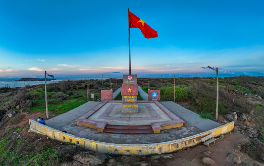 The national flagpole on Phu Quy island was built in Trieu Duong village, Tam Thanh commune with a height of 22.6 m, reinforced concrete, facing the sea. The architecture of the building consists of pillars, flagpoles, steps and surrounding grounds. The foundation is buried deep under the rock with the foundation structure technique commonly used for solid lighthouses. The 4 x 6m fabric flag is sewn with sustainable fabric with characteristics of sea breeze. The flagpole on Phu Quy island is like a solid sovereignty stele in the middle of the sea, affirming Vietnam's maritime territory.
