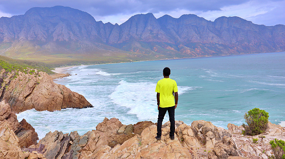 Young black African man standing on a cliff close to the ocean