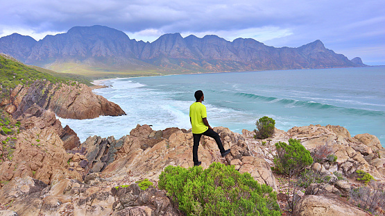 Young black African man standing on a cliff close to the ocean