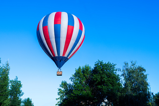 a hot air balloon flying near the trees on a blue sky. air transport against the sky
