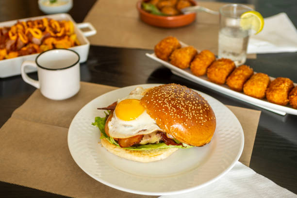 istock Burger with fried egg, fried bacon and melted cheese served in a tapas restaurant with other dishes such as croquettes and chorizos to hell 1488133540