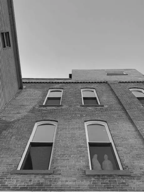 Black and white photo, looking up at an old architectural building in downtown Marinette, Wisconsin. Taken from below on the city streets. Statue of Marie and Joseph can be seen in one window on the building.