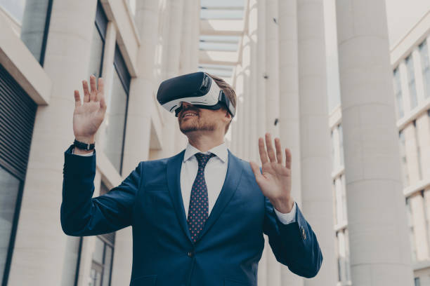 istock Man in formal blue suit walking around in virtual reality while wearing VR goggles 1488143176