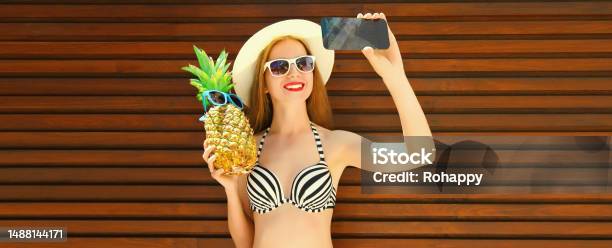 Summer Portrait Of Happy Smiling Woman Holding Pineapple Taking Selfie With Smartphone Wearing Straw Hat Sunglasses Bra Stock Photo - Download Image Now