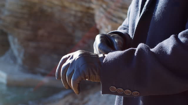 Man in dark coat puts on black leather gloves walking away