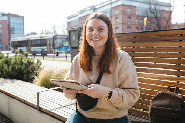 istock Beautiful smiling female student using tablet outdoors. Happy cheerful young woman siting on the bench on city street, Urban lifestyle concept. Online education or shopping banner 1488147102