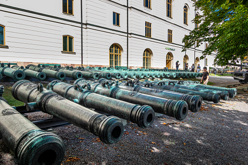 Stockholm, Sweden - August 10, 2022: Beautiful perspective view of many ancient iron cannons outside the public Army museum with incidental people in Stockholm Sweden August 10, 2022.