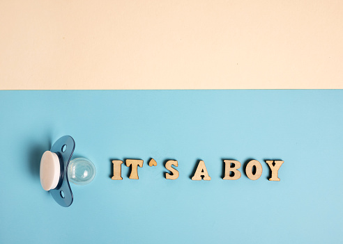 its a boy inscription from wooden letters, ultrasound picture pacifier flat lay