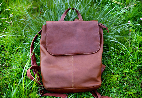 woman with brown bag backpack outside on park bench.bag in green grass or outside rock stone