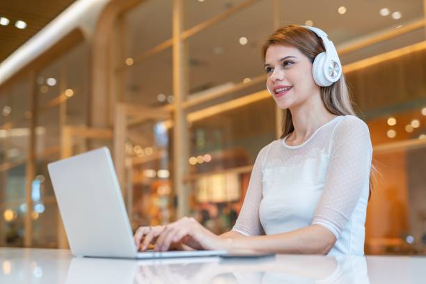 istock Casual businesswoman using laptop and headphone doing e-learning and video conferencing from a workspace with cafe 1488165240