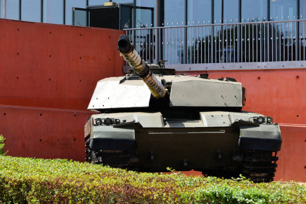 A wide-angle front view of a Japanese self-defense force military tank driving down a dirt road lined with trees with a dramatic sky.