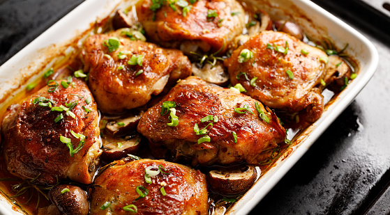 Roasted chicken thighs seasoned with garlic and herbs in a baking dish, close-up