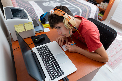 Teenage boy is studying via pc. The boy doing his homework on the computer in his room is holding a live conference.