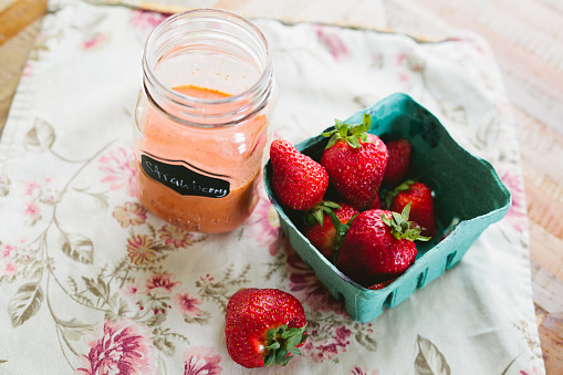 Jar of homemade strawberry vinaigrette beside a basket of fresh strawberries on a table