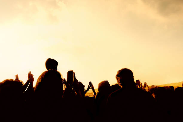 Silhouetted people over sunny sky at live event