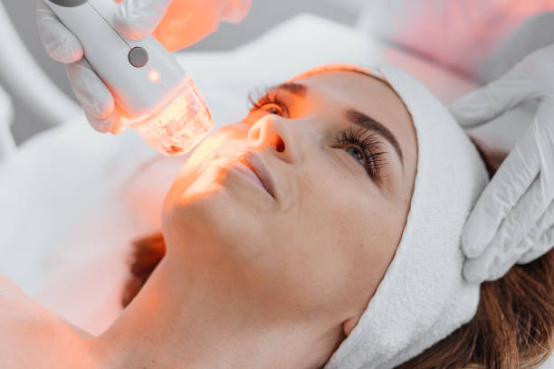 Photo from the studio of cosmetology, demonstrating the process of led therapy and facial skin care. A woman undergoes a procedure in a beauty salon. Beautician in white gloves use Photo from the studio of cosmetology, demonstrating the process of led therapy and facial skin care. A woman undergoes a procedure in a beauty salon. Beautician in white gloves use. High quality photo light therapy stock pictures, royalty-free photos & images