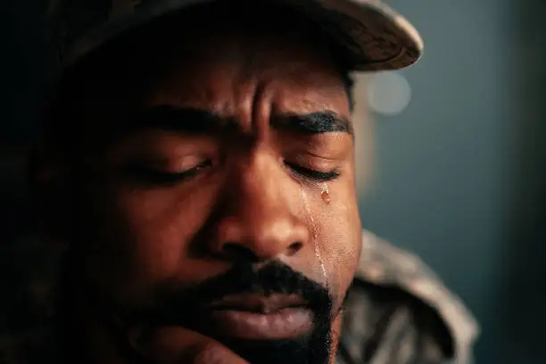 A close up shot on the face of an African American soldier in uniform crying.