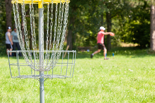 Disc golf player throwing a flying disc in the park, chain basket in the focus