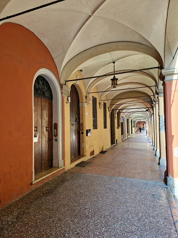 Portico in bright yellow or orange (light) colors in Bologna, Italy, with marble floor and arched stone walls - lantern hanging on ceiling and wooden gate