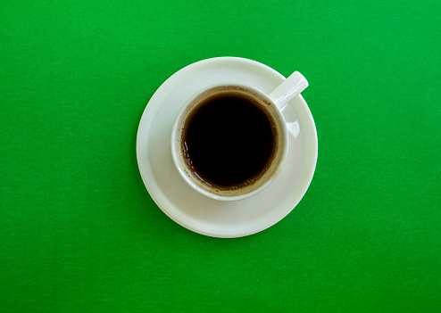 Cup of coffee on a green background, top view. Cup of coffee with a saucer on a green background, top view.