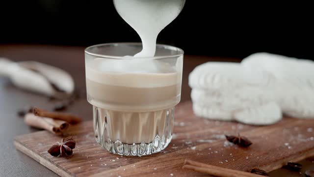 Glass with Cappuccino and white Cakes with cream on wooden board. Slow motion of pouring Milk into Coffee drink on brown background
