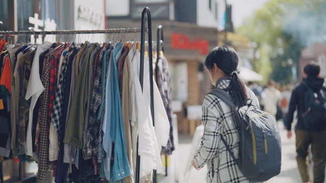 Young asian  woman choosing shirt on rack in showroom in the 2nd hand market.