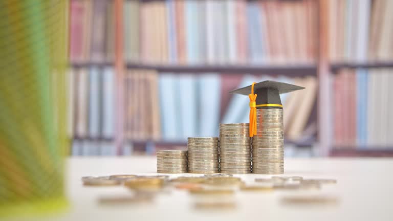 Tuition payment or tuition fee, expense for graduate study abroad program concept : Black graduation cap on stacks of coins, depicting fees charged by education institution for instruction or services