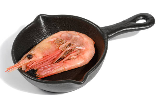 Boiled shrimp in a miniature black pan on a white background