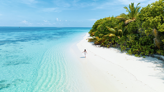 Aerial drone view of a woman walking on desert island in Maldives