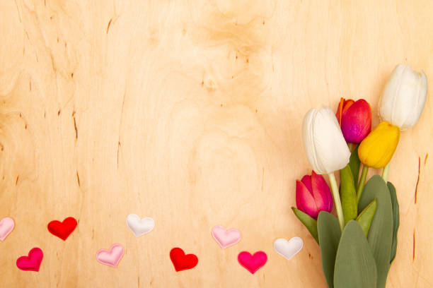 Tulip flowers and small herts on wooden background with copy space. Love charm meets floral enchantment.