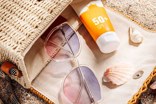 Sunscreen and glasses in a wicker straw bag on a sandy beach