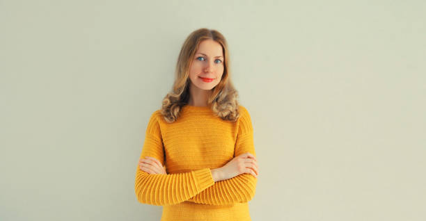 ritratto di bella giovane donna in maglione giallo a maglia con le braccia incrociate su priorità bassa grigia della parete - human lips orange lipstick human mouth foto e immagini stock