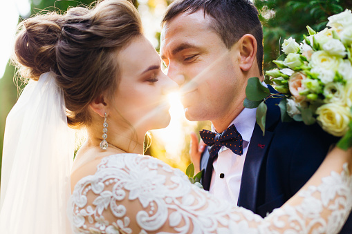 the bride and groom closed their eyes and want to kiss and sunlight between their faces. park.