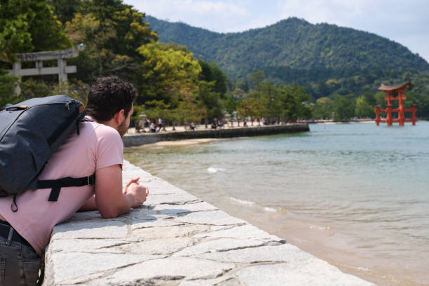 turista europeu visita itsukushima jinja otorii no mar de miyajima, japão. - jinja - fotografias e filmes do acervo